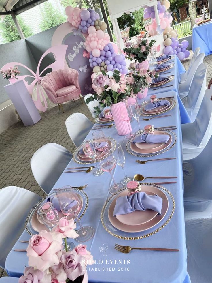 a long table with plates and flowers on it in a room filled with blue chairs