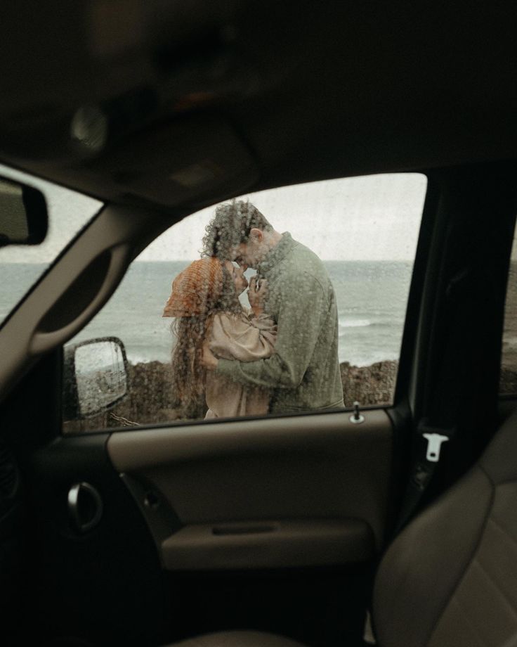 a man and woman kissing in the back seat of a car next to the ocean