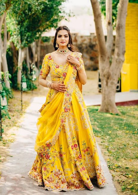 a woman in a yellow dress standing on a sidewalk with trees and grass behind her