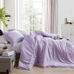 a bed covered in purple sheets and pillows next to a potted plant on top of a dresser