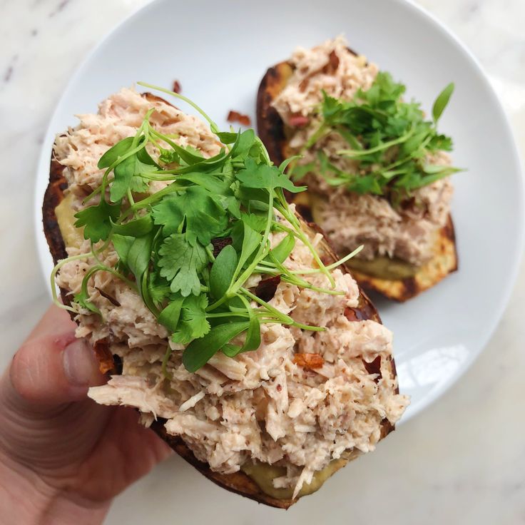 a hand holding a sandwich with meat and veggies on it while sitting on a white plate