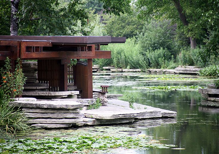 there is a small structure in the middle of water surrounded by plants and rocks,