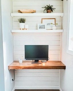 a desk with a computer on top of it in front of a white shipboard wall