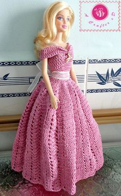 a barbie doll wearing a pink crocheted dress and matching shoes is posed on a table