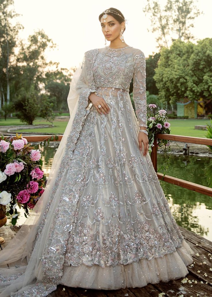 a woman in a wedding dress standing on a bridge with flowers and trees behind her