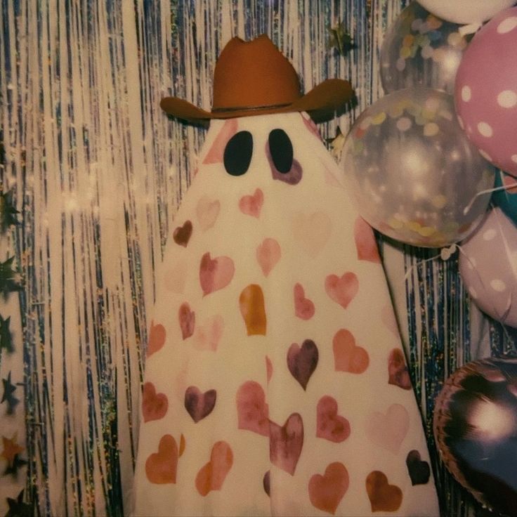 a white dress with hearts on it and a cowboy hat is next to some balloons