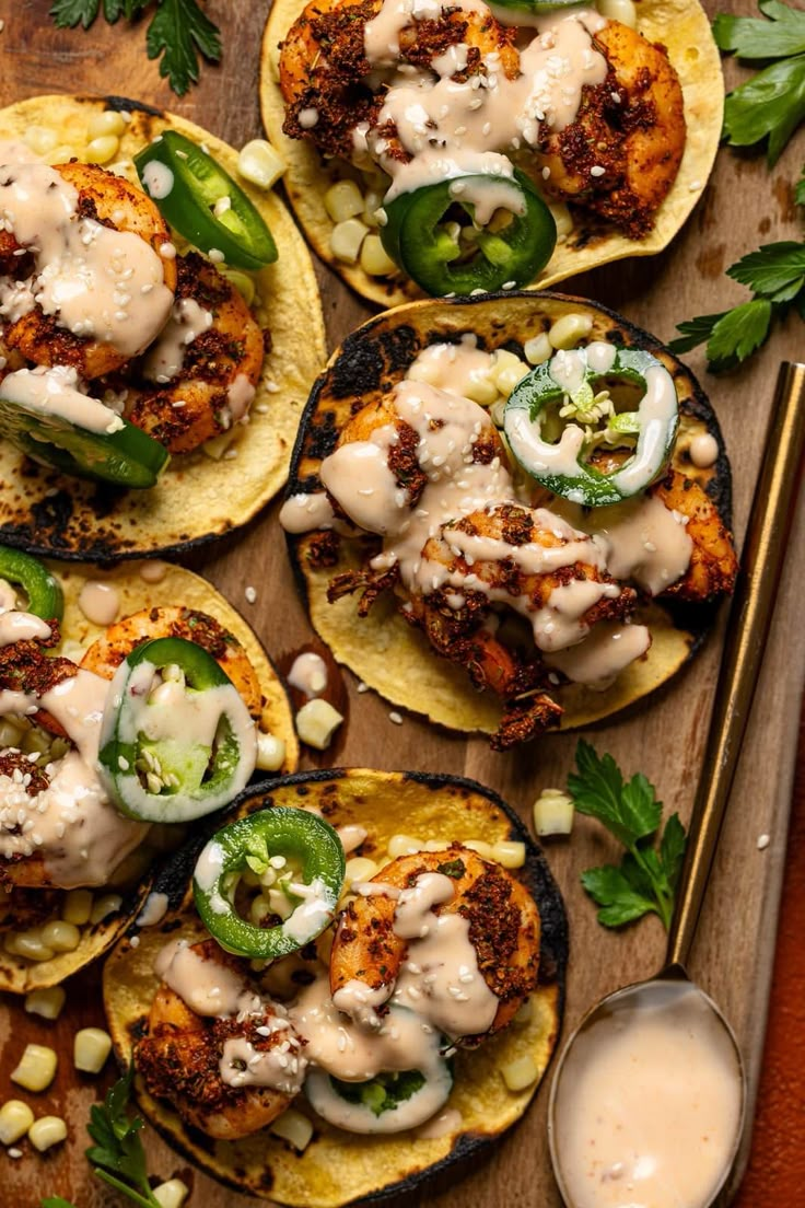 several tacos with meat and vegetables on them, sitting on a cutting board next to some dipping sauce