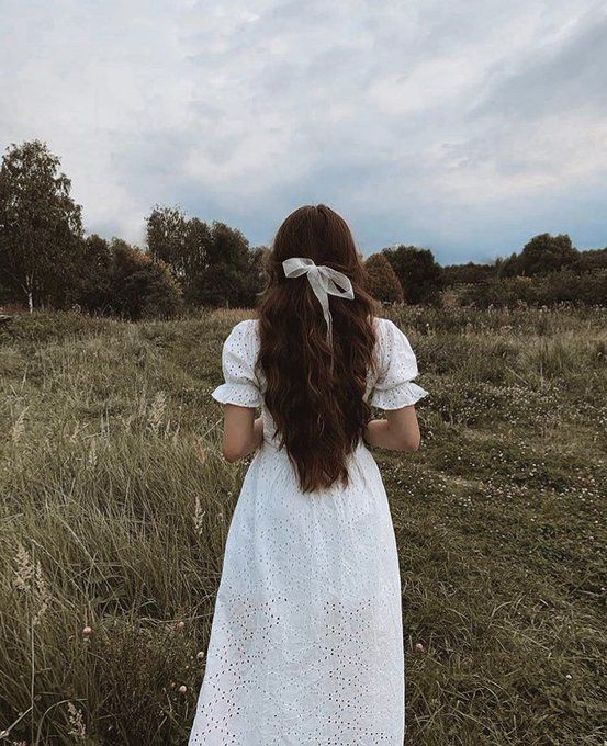 a woman standing in a field with her back to the camera, wearing a white dress