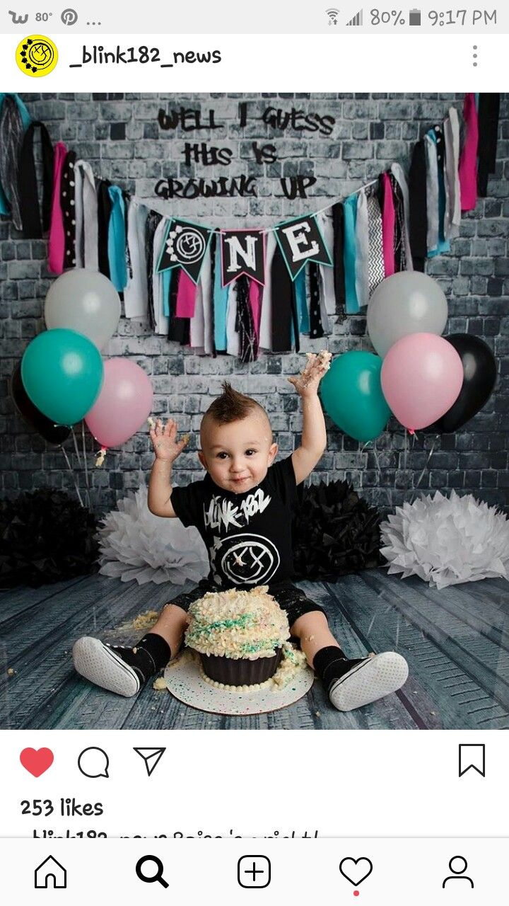 a little boy sitting on top of a cake in front of balloons and streamers