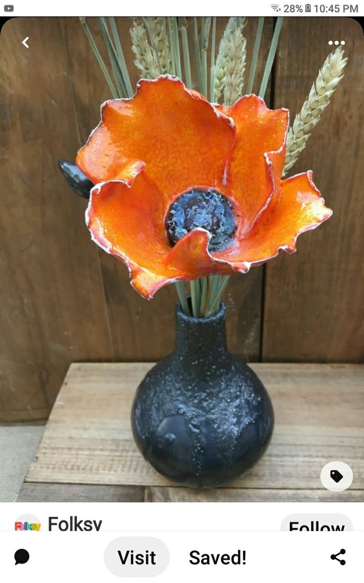 an orange flower is in a black vase