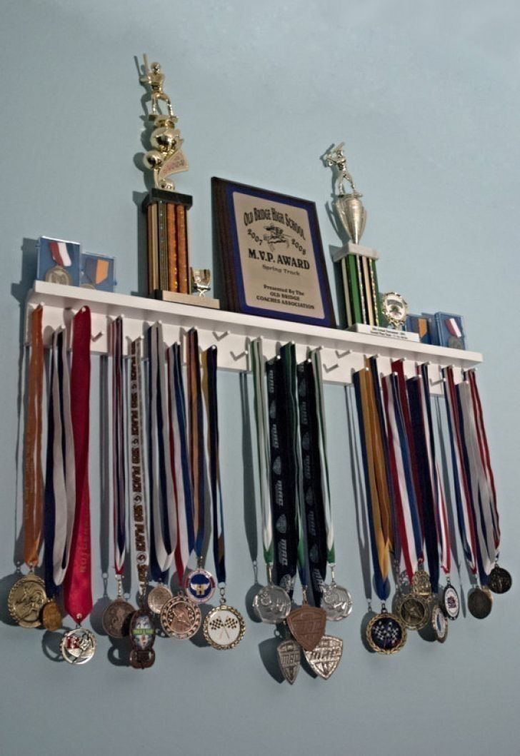 a wall mounted shelf with medals and trophies hanging from it's sides in front of a blue wall