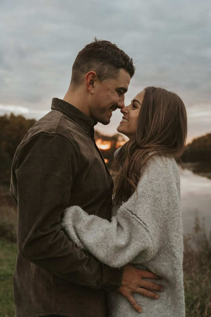 a man and woman standing next to each other in front of a body of water