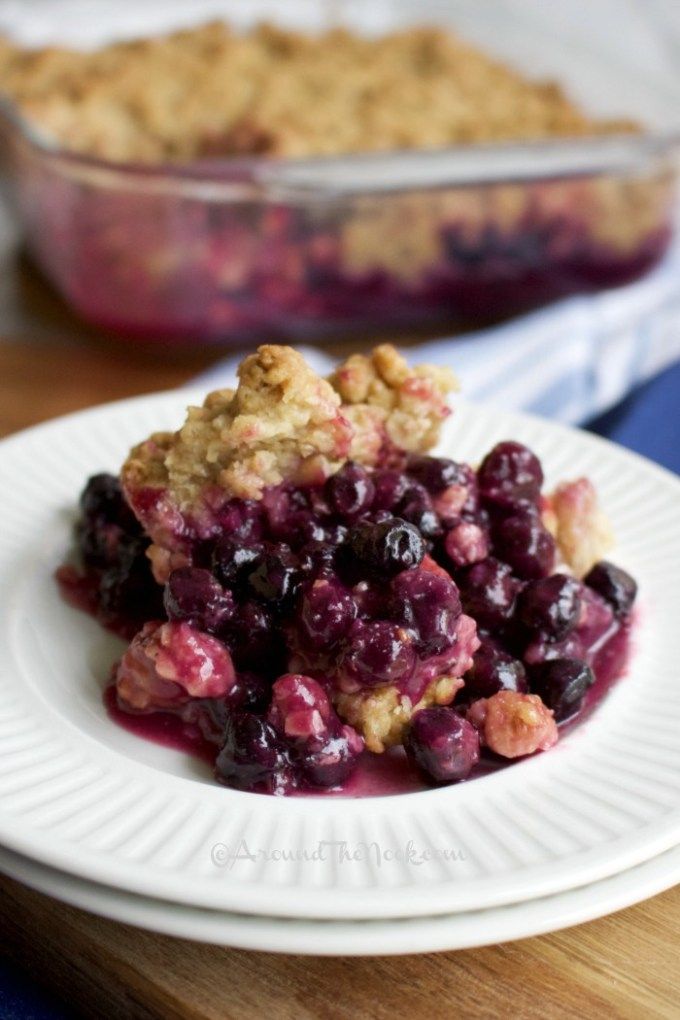 a white plate topped with blueberry cobbler next to a glass dish