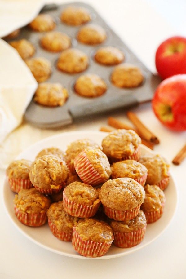 a plate full of muffins next to an apple and cinnamon stick on a table