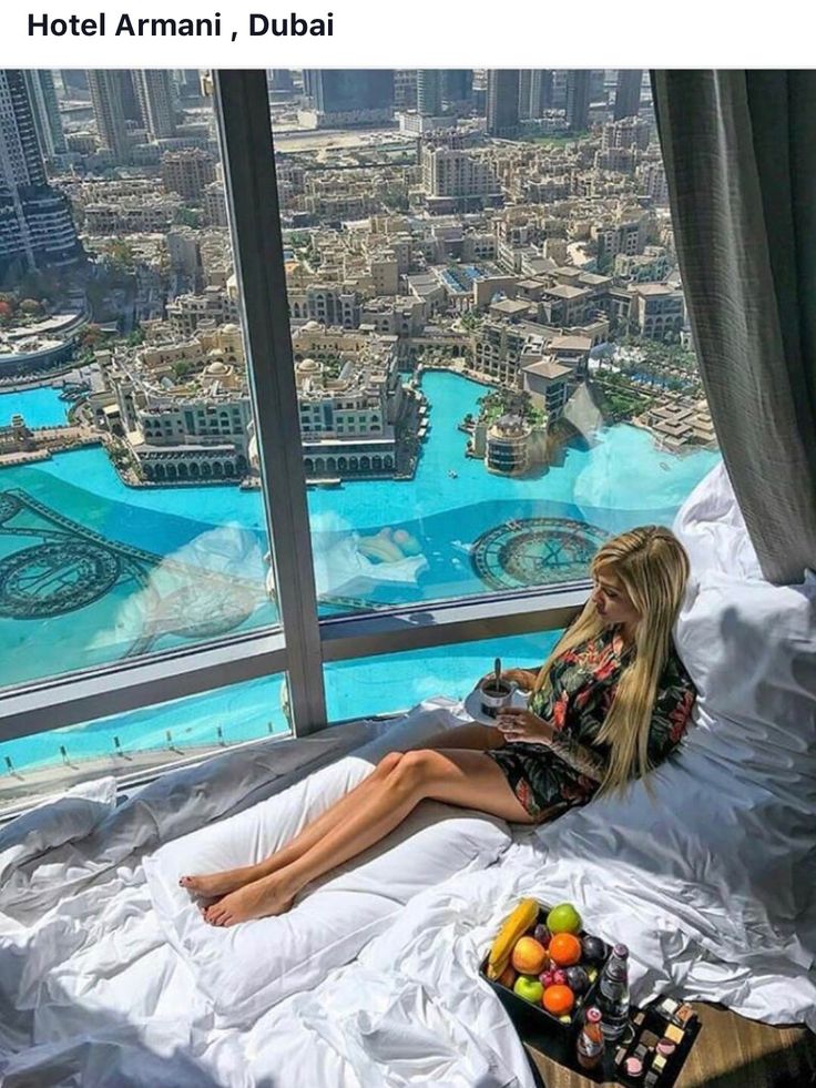 a woman sitting on top of a bed in front of a window overlooking the city