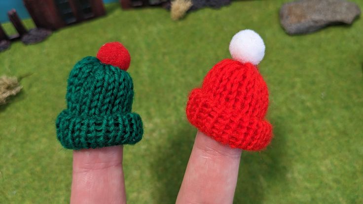 two knitted christmas hats sitting on someone's finger