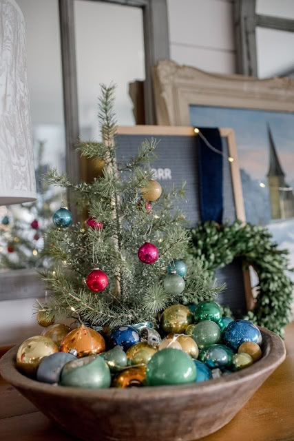 a wooden bowl filled with ornaments on top of a table next to a christmas tree