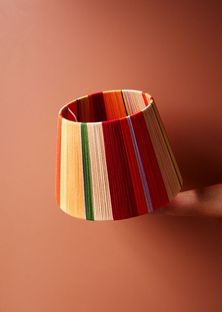 a colorful lamp shade hanging from the side of a pink wall in front of a person's hand