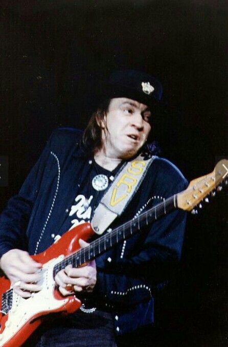 a man playing an electric guitar in front of a black background with his hat on