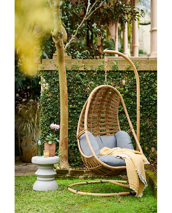 a hanging chair in the grass with a blanket on it's back and a potted plant next to it