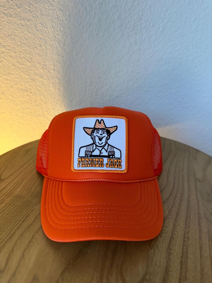 an orange trucker hat with a cartoon character on the front and back, sitting on top of a wooden table