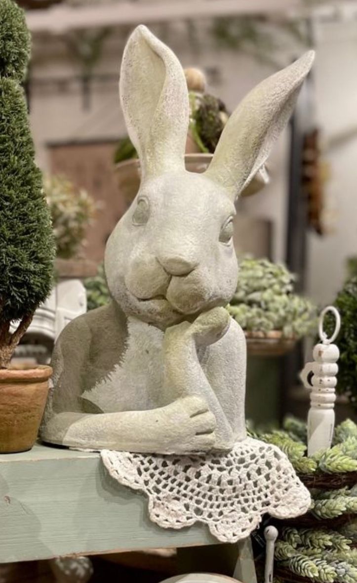 a statue of a rabbit sitting on top of a table next to potted plants