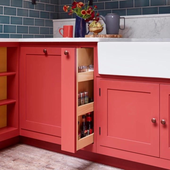 an open cabinet in the middle of a kitchen with red cabinets and white counter tops