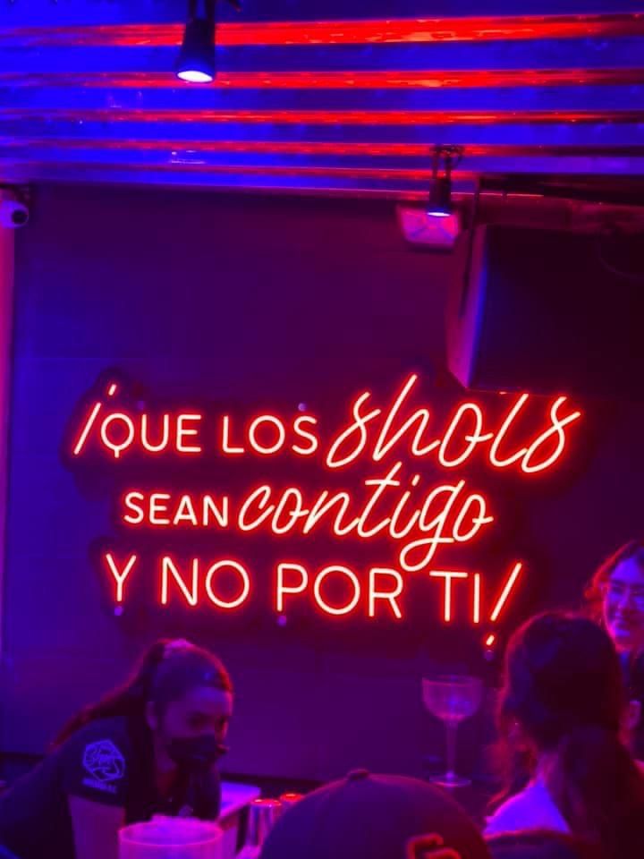 a neon sign is lit up in front of a group of people at a bar