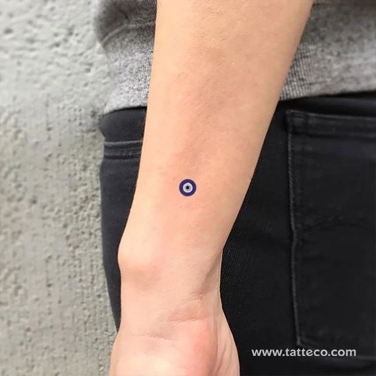 a woman's arm with a small blue dot tattoo on the left side of her wrist