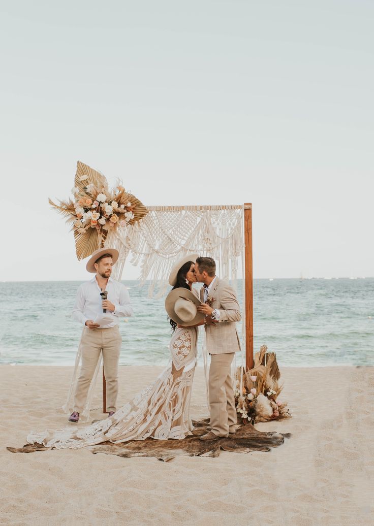 a couple getting married on the beach in front of an arch decorated with flowers and feathers