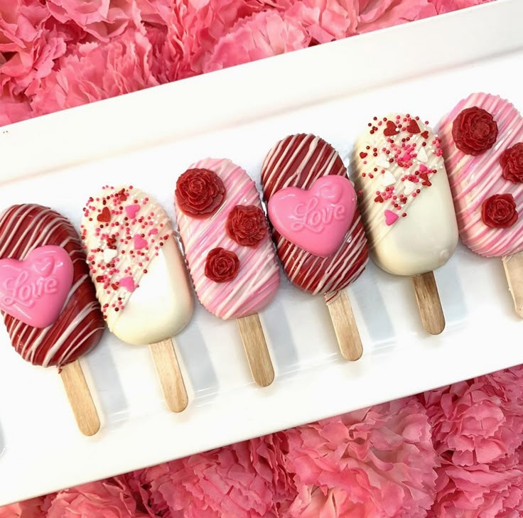 four heart shaped lollipops sitting on top of a white plate next to pink flowers