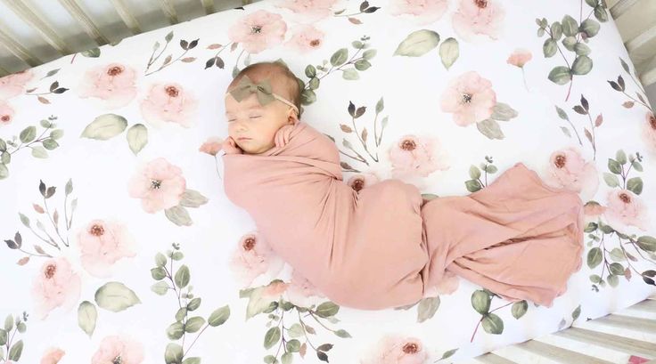 a baby sleeping in a crib with pink flowers on it