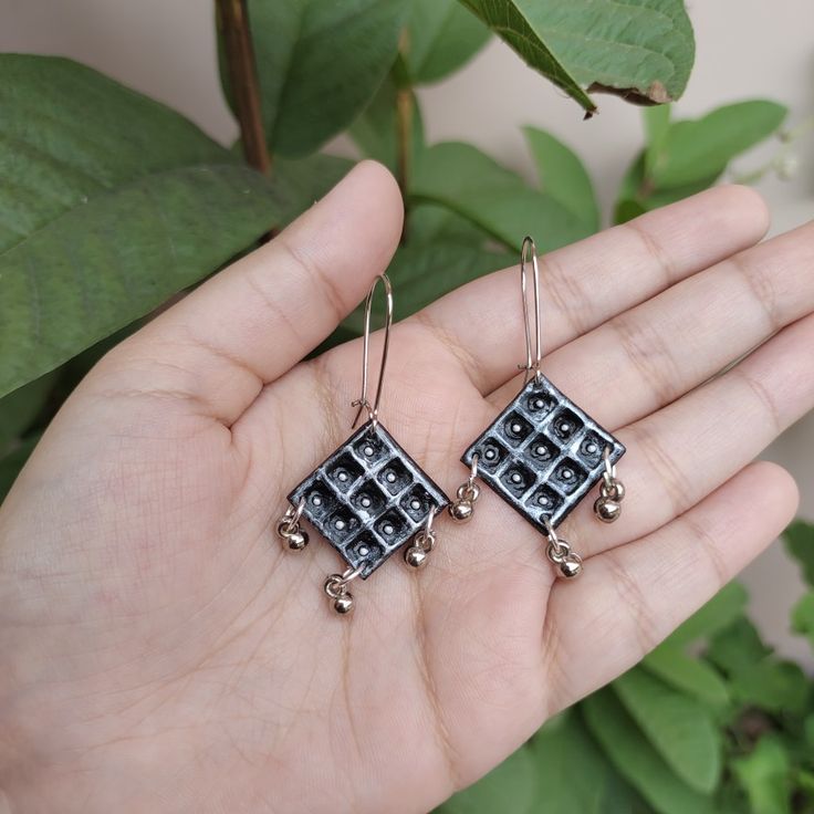 a pair of black and white square shaped earrings on a person's left hand