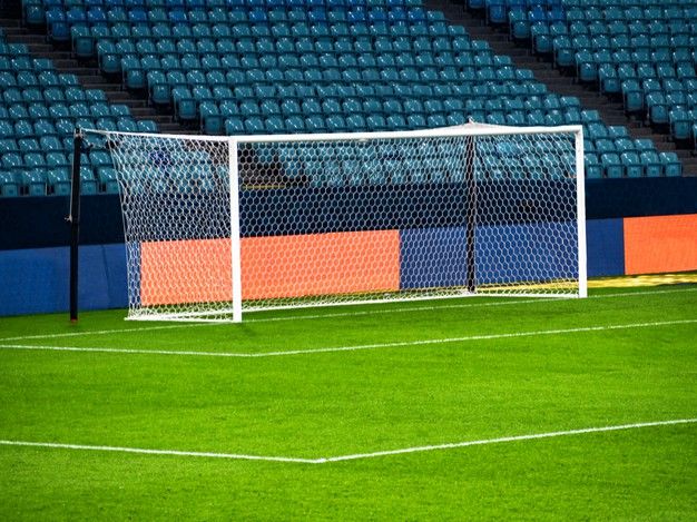 an empty soccer field with a goal in the middle and blue stadium seats behind it