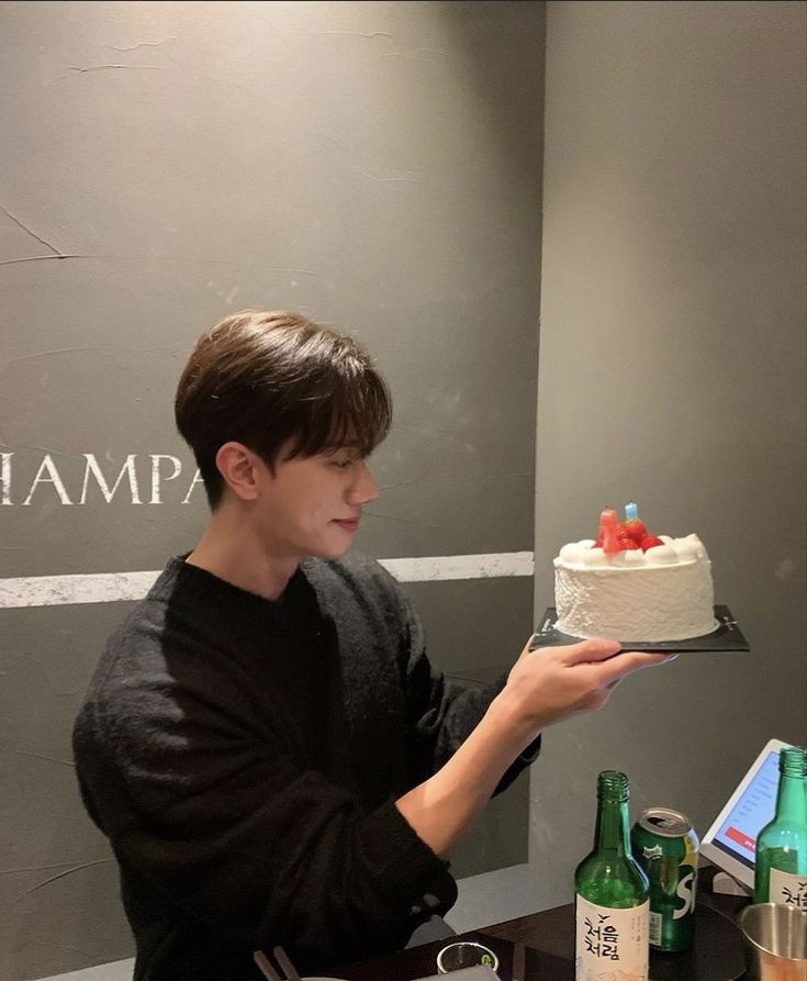 a young man holding a cake on top of a table