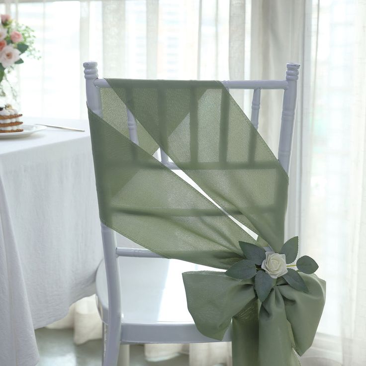 a white chair with a green bow on it next to a table covered in flowers