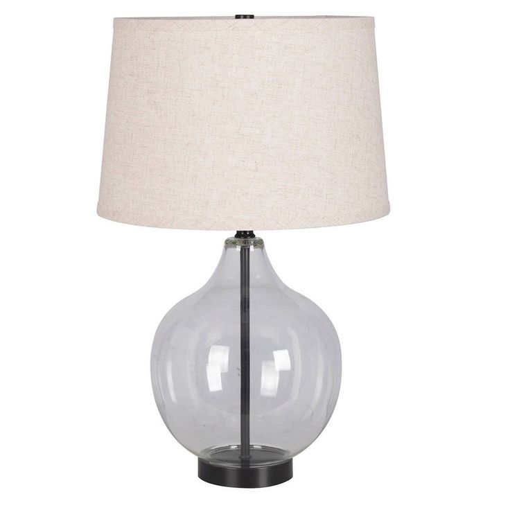 a clear glass table lamp with a beige linen shade on the bottom and black base