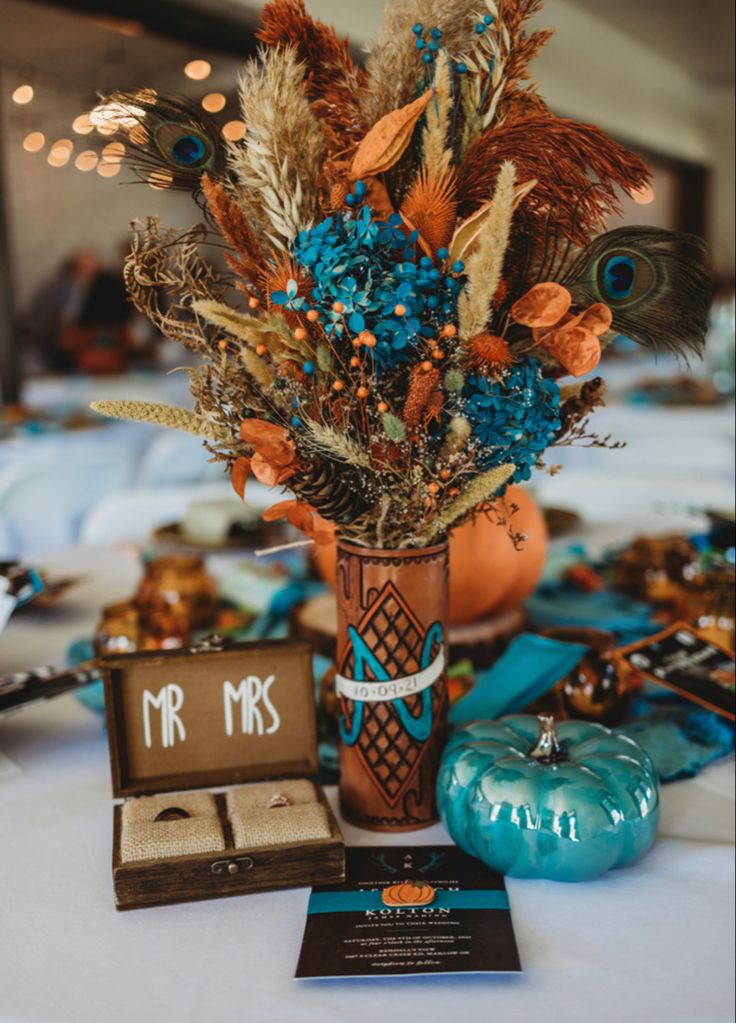 an arrangement of flowers and feathers in a vase on a table at a wedding reception