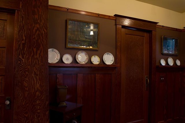 plates are arranged on the wall in front of wooden paneling and framed pictures above them