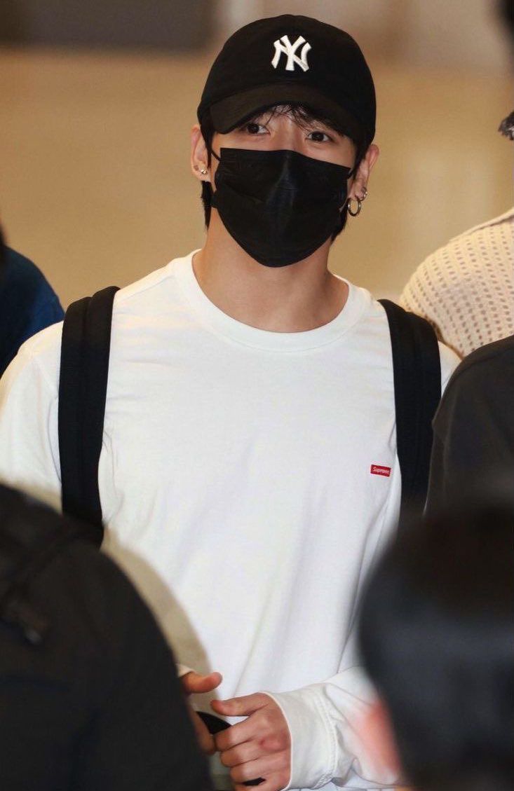 a man wearing a black face mask and backpack at an airport with other people in the background