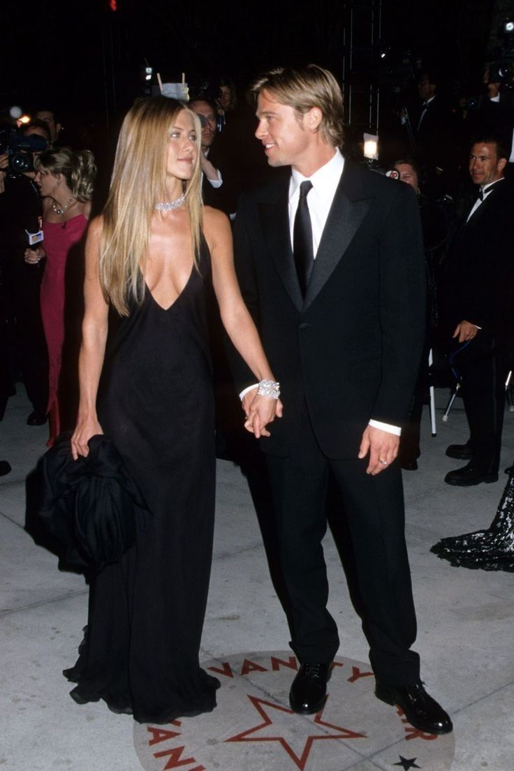 a man in a tuxedo and a woman in a black dress holding hands