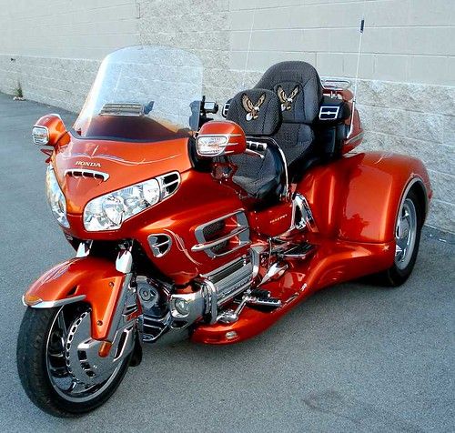 an orange motorcycle parked next to a white wall and cement flooring in a parking lot