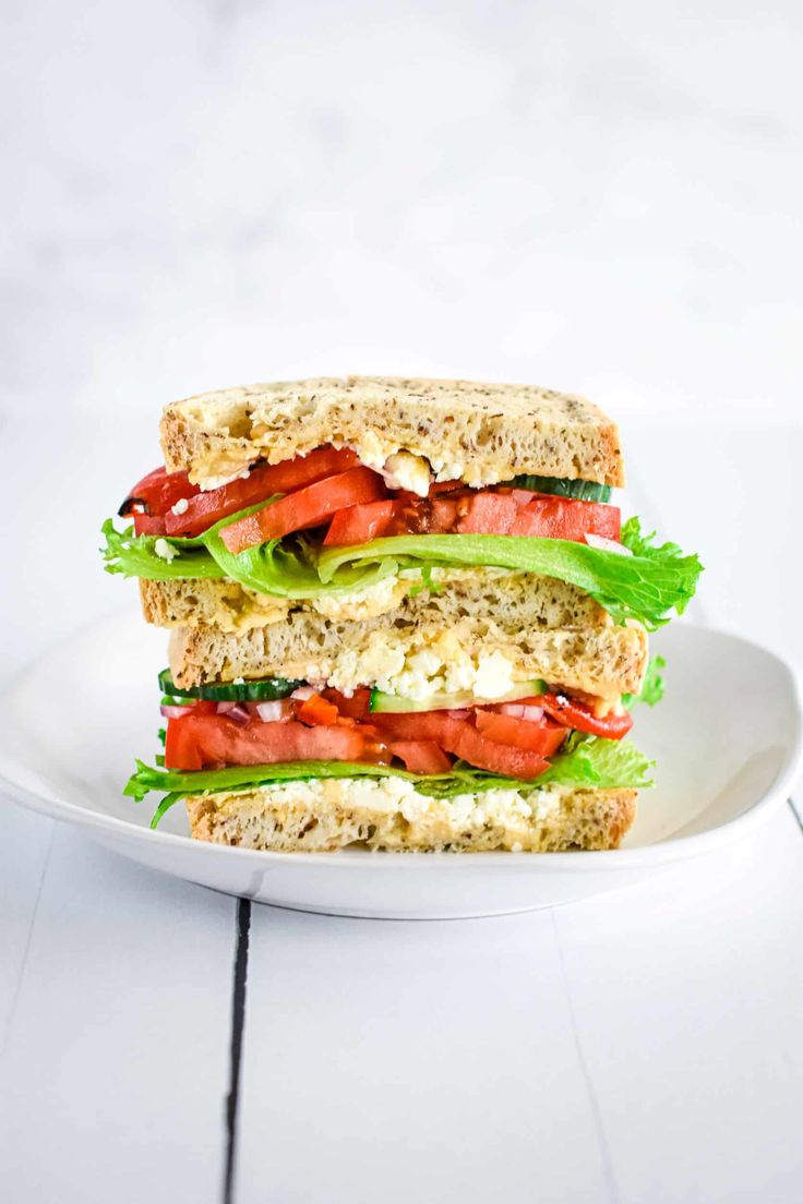 two halves of a sandwich stacked on top of each other with lettuce and tomatoes