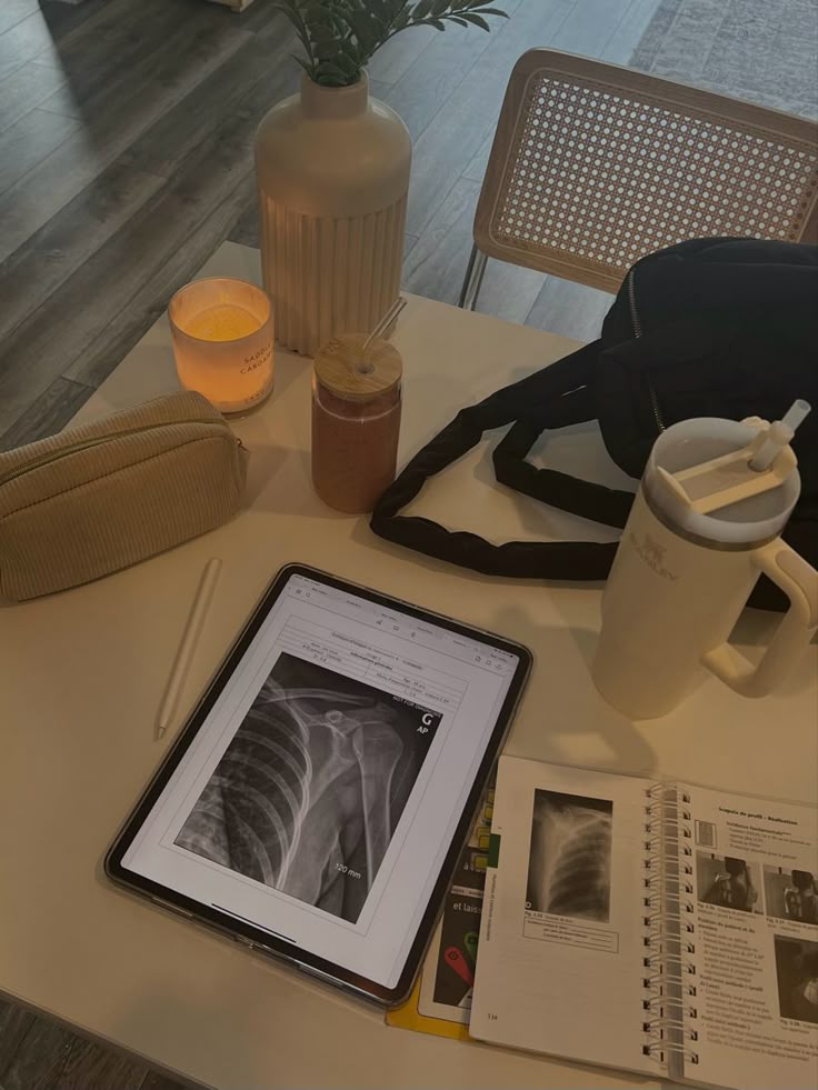 a tablet computer sitting on top of a table next to a vase and cup filled with liquid