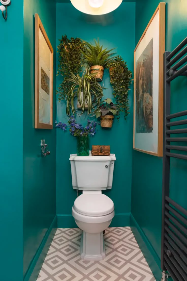 a white toilet sitting in a bathroom next to a green wall and potted plant