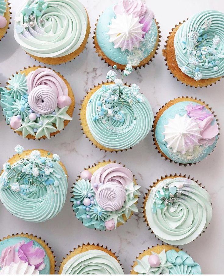 cupcakes decorated in pastel blue and pink frosting on a marble surface