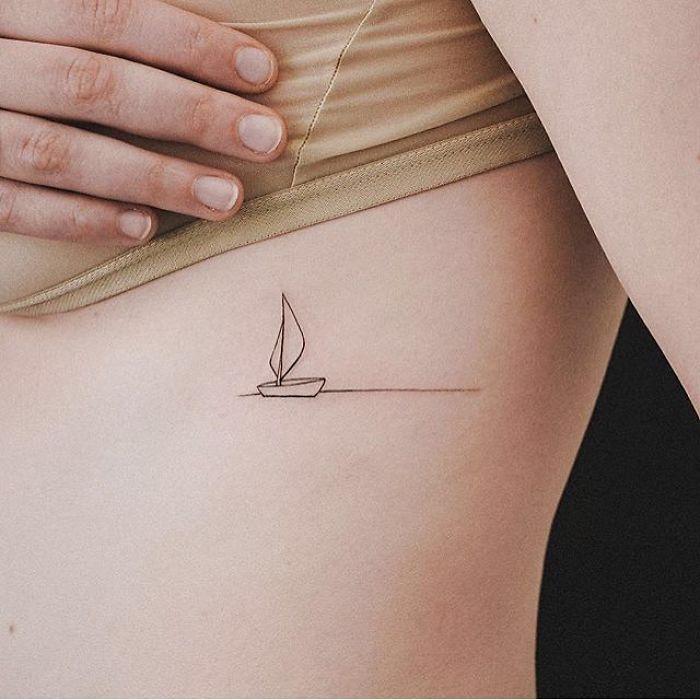 a woman's stomach with a small sail tattoo on her left side ribcage