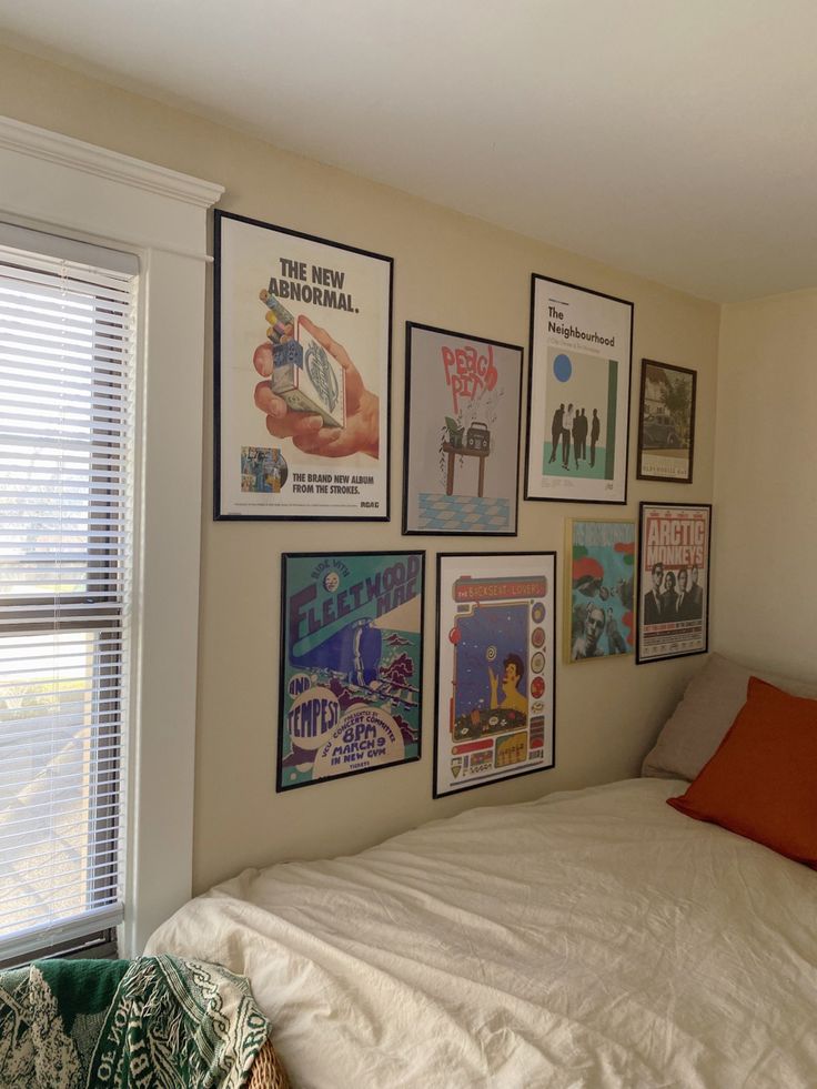 a bedroom with posters on the wall and a white bed in front of a window