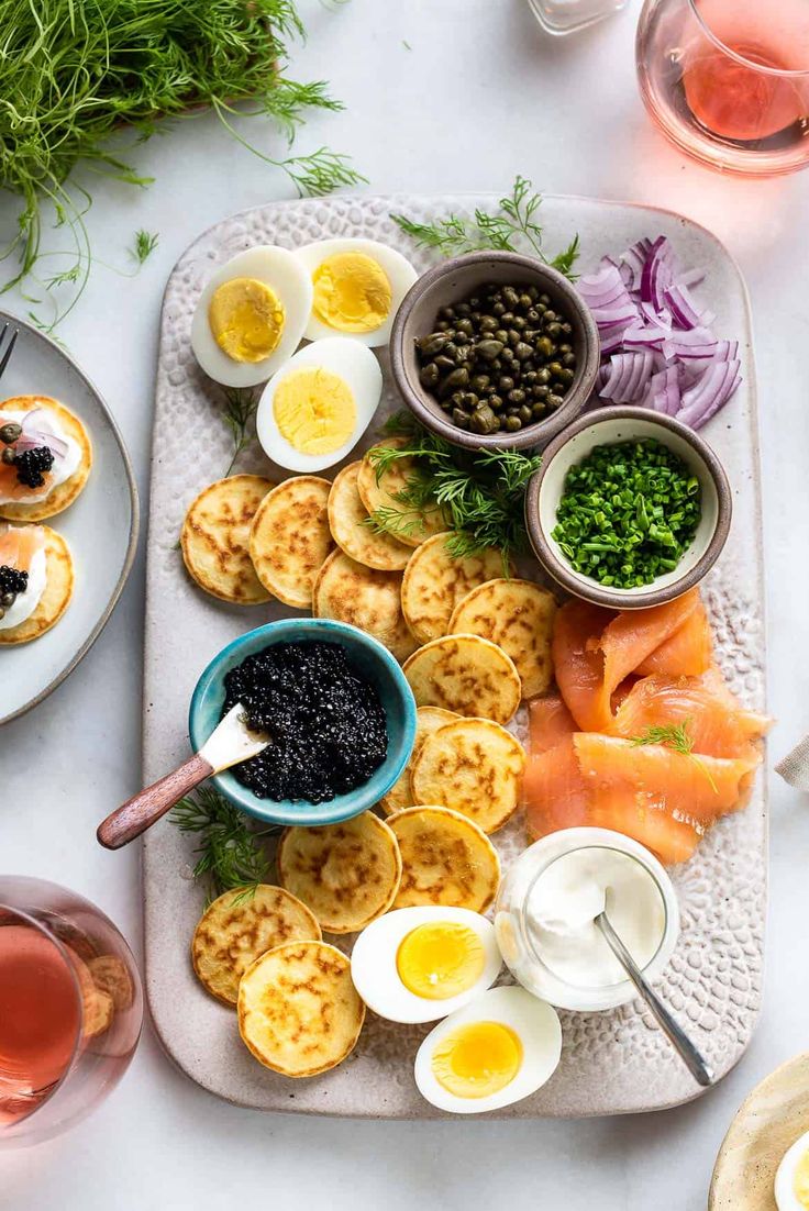 an assortment of food on a platter with wine glasses and utensils next to it