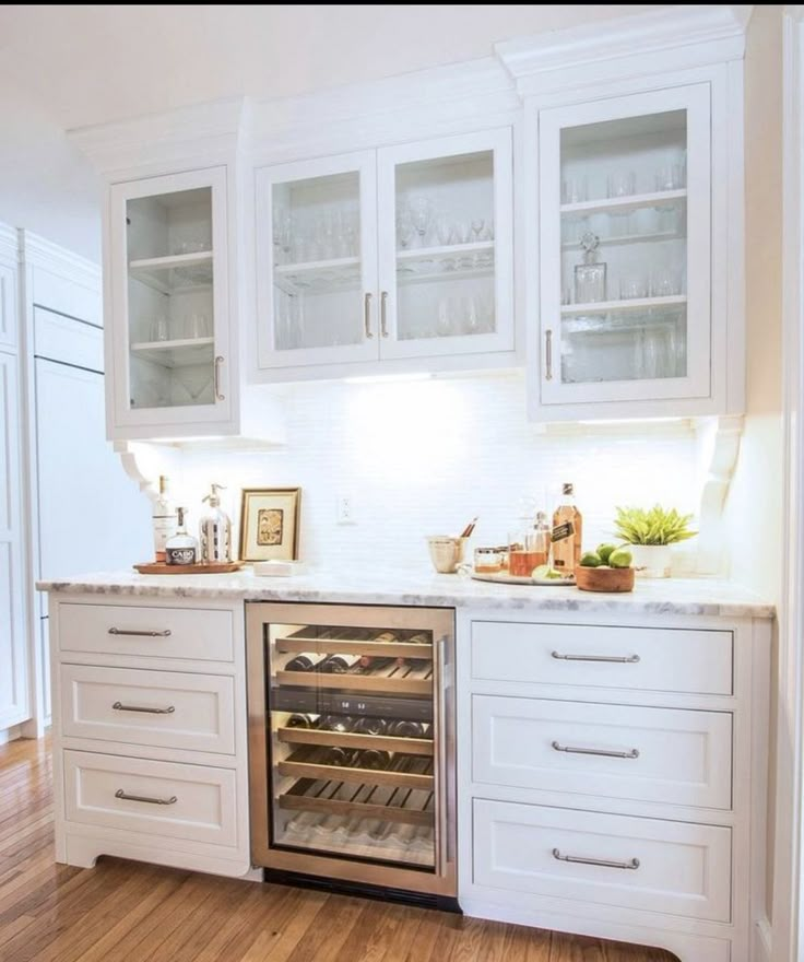 a kitchen with white cabinets and wood flooring has an oven in the center, built - in wine cooler